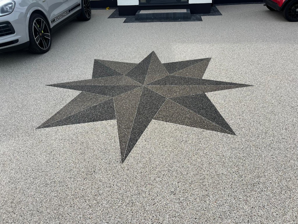 Resin-bound driveway with an inlaid dark compass-star motif and block edging at the entrance