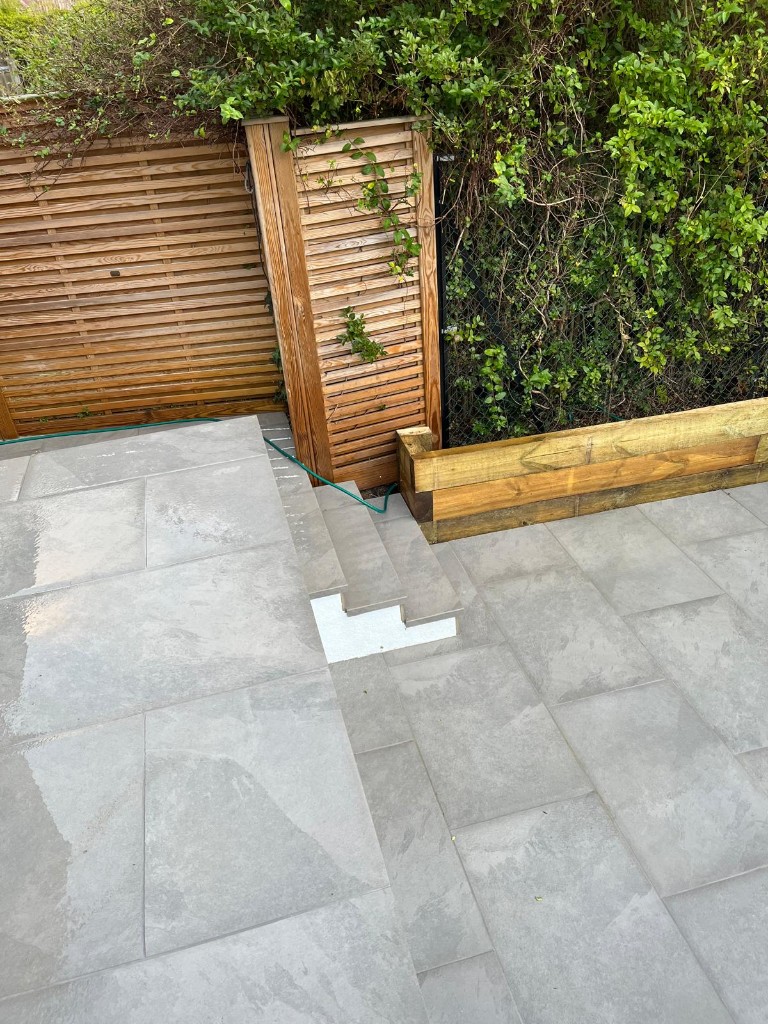 Split-level grey stone patio with sleeper retaining detail and slatted timber fencing