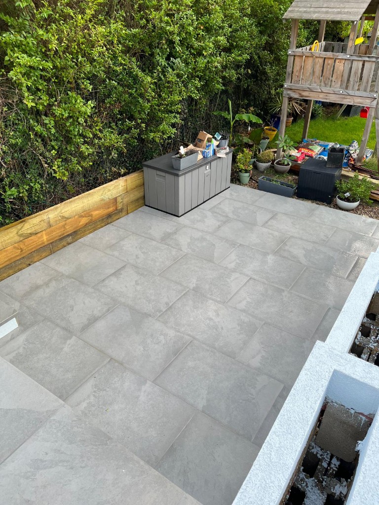 Grey stone patio slab layout beside sleeper edging and dense garden hedge