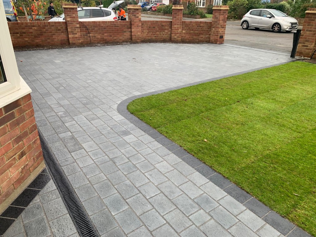 Residential driveway with light grey block paving, charcoal border edging, integrated drainage and a neatly edged lawn
